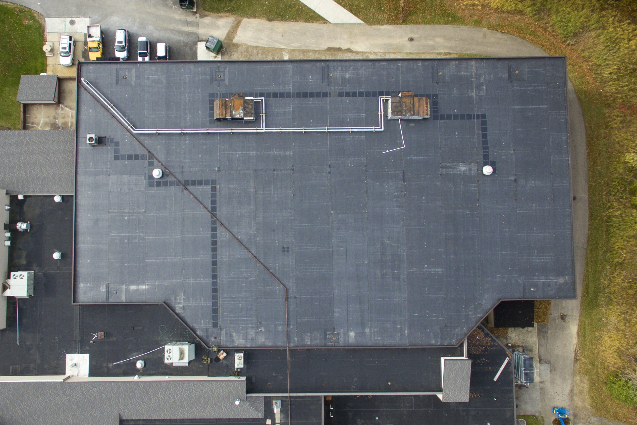 Aerial view of a large black commercial flat roof with HVAC units and piping, showcasing comprehensive commercial roof maintenance in Akron by Tusing Builders.