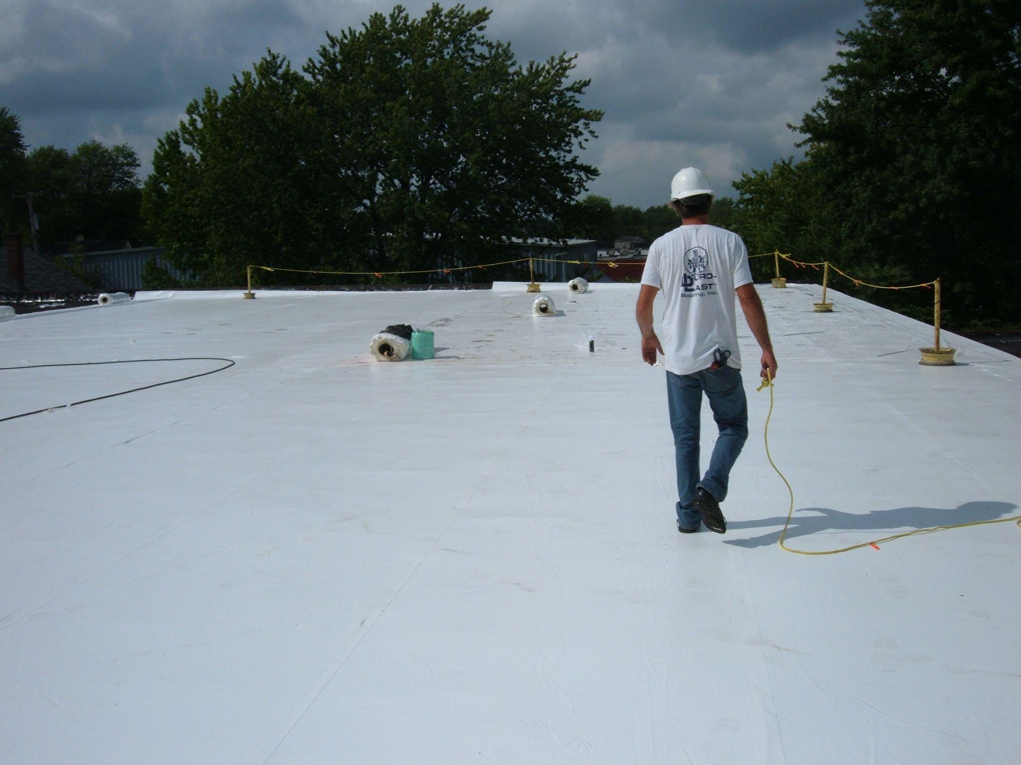 Roofing professional walking across a large, newly installed white flat membrane system, showcasing the precision of Industrial Roofing in Youngstown OH by Tusing Builders.