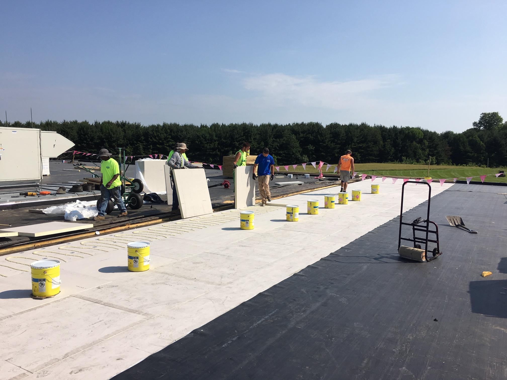 Tusing Builders crew installs rigid insulation boards on a large commercial roof project, demonstrating the technical layers of Industrial Roofing in Youngstown OH.