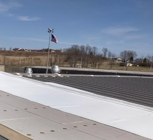 Field photo of a large-scale commercial roofing project in Akron, OH by Tusing Builders, showing the installation of a high-reflectivity white membrane over a metal deck to create a monolithic, energy-efficient building envelope.