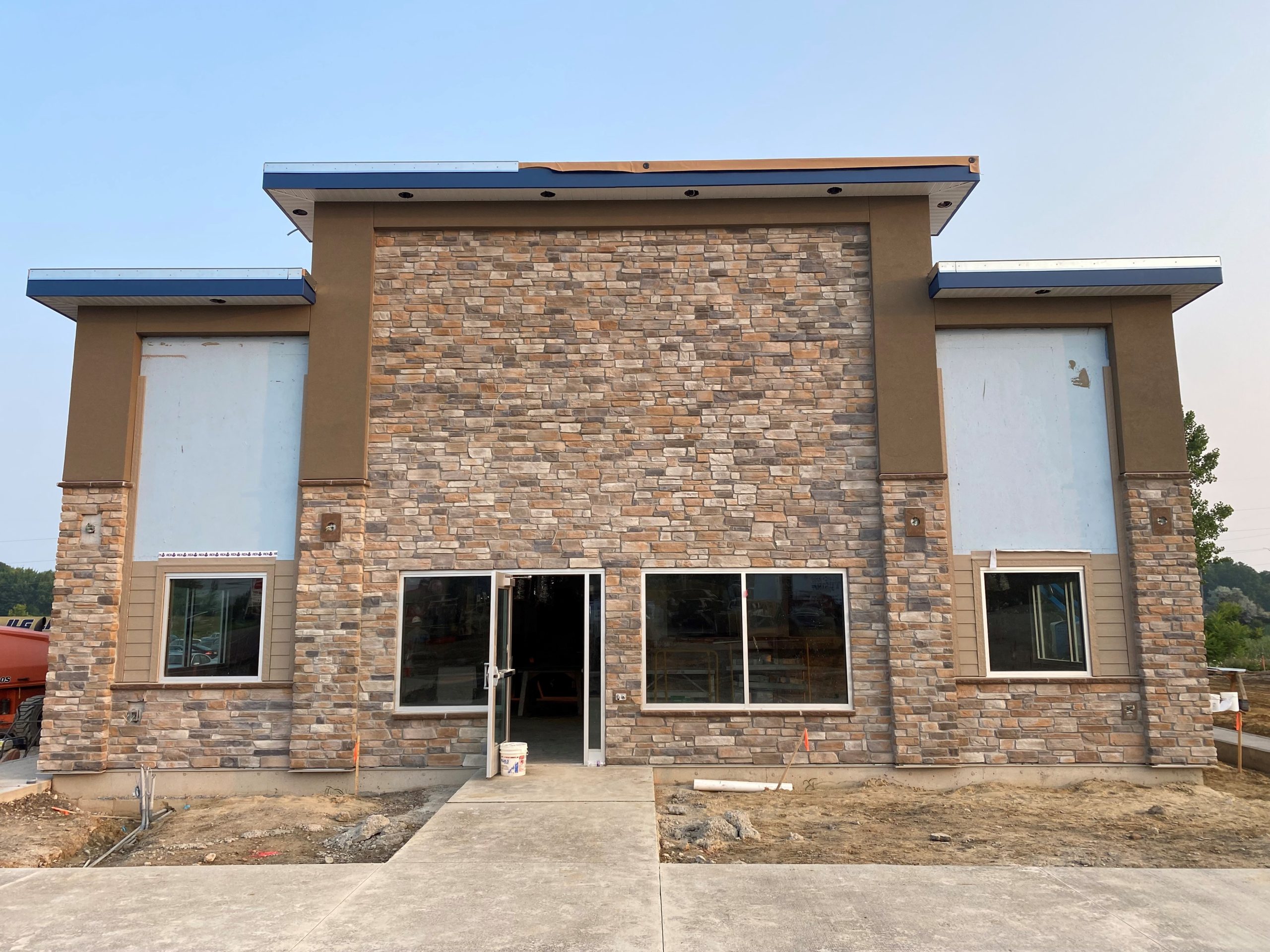 Technical site photo by an Ohio commercial roofing company, Tusing Builders & Roofing, showing the final architectural detailing and building envelope integration on a commercial facility featuring a stone masonry facade and tiered rooflines.
