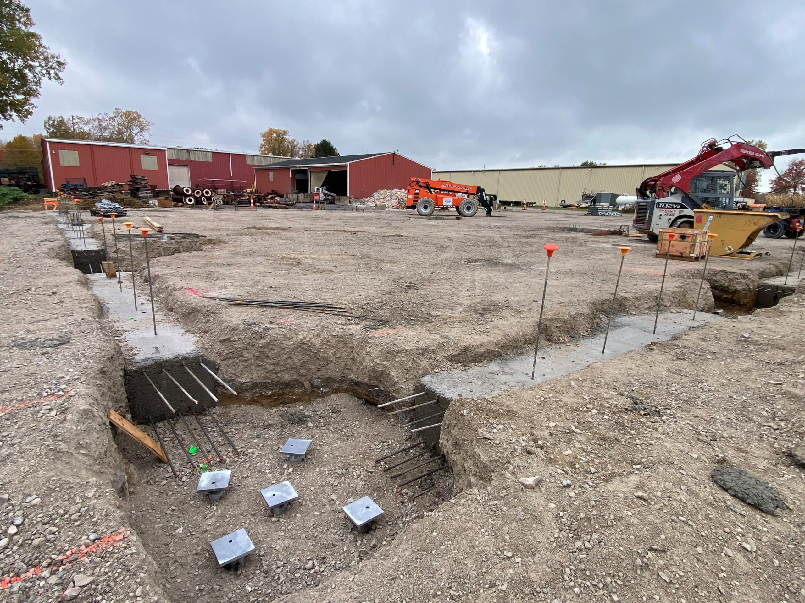 Ground-level site photo by an Ohio commercial roofing company, Tusing Builders & Roofing, showing the precision excavation and concrete footing phase of a new building project, featuring reinforced steel rebar and industrial site preparation.