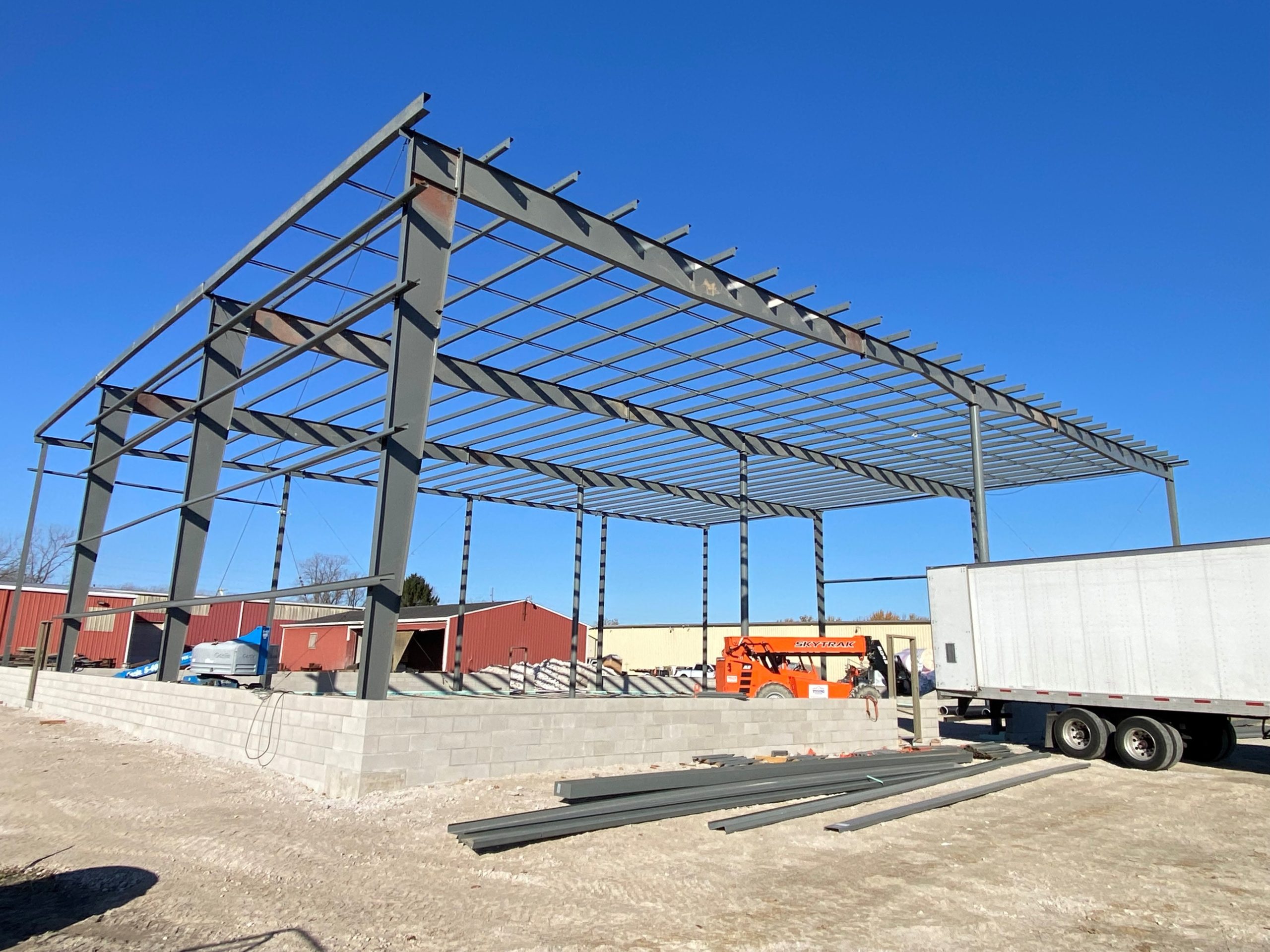 Technical site photo by an Ohio commercial roofing company, Tusing Builders & Roofing, showing the structural steel framing and roof joists of a new industrial building being integrated with a precision-laid masonry foundation.